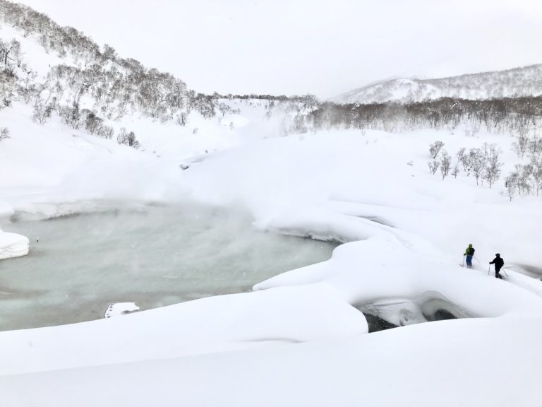 Deux skieurs de randonnée près d'une source chaude fumante dans un paysage enneigé, région de Niseko, Japon.